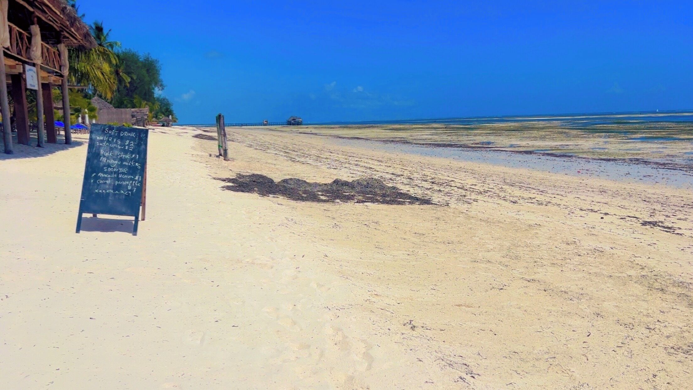 A beach with a sign listing soft drinks and prices.