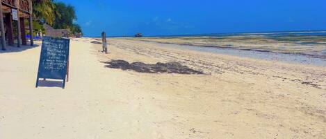 A beach with a sign listing soft drinks and prices.