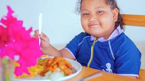Un enfant est assis à une table en bois, devant une assiette de nourriture et une fourchette.