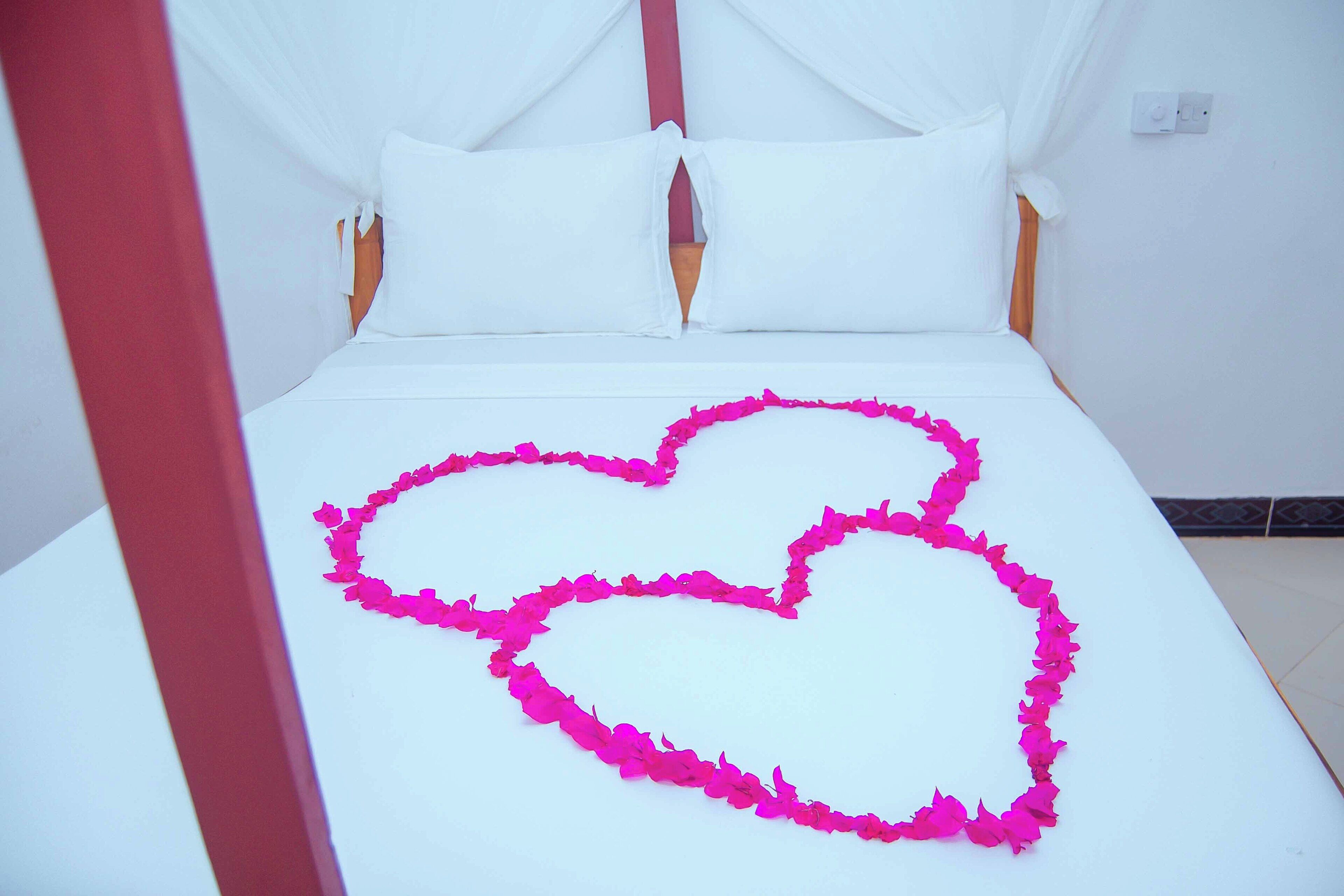 A bed with a white canopy and pink flower petals arranged in a heart shape.
