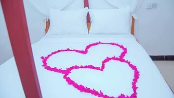 A bed with a white canopy and pink flower petals arranged in a heart shape.
