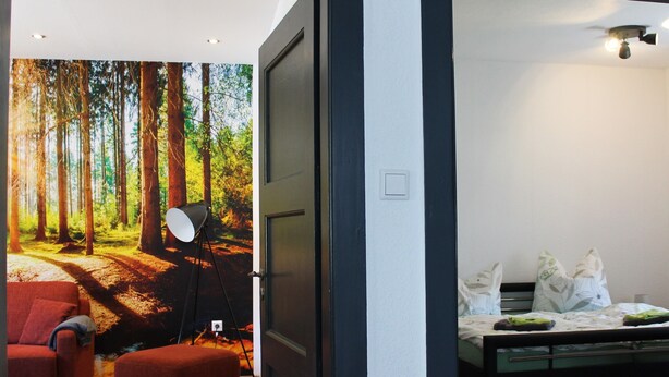 Un dormitorio con una cama, una mesita de noche, un sofá rojo y un gran mural de un bosque en la pared.