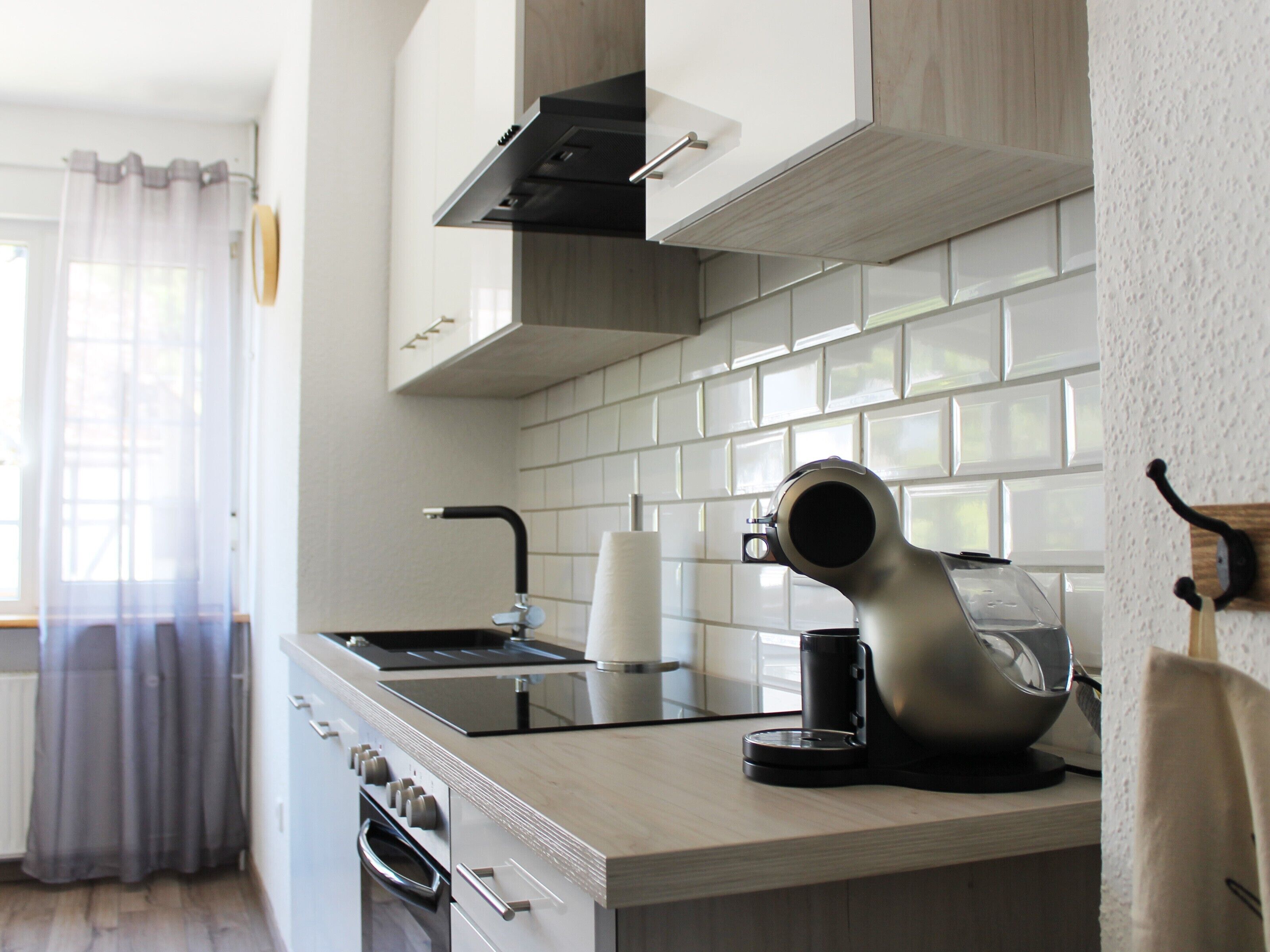 A modern kitchen with white cabinetry, a stainless steel range hood, a coffee maker, and a kettle on the counter.