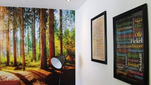Una habitación con un mural de un bosque, una nube de palabras enmarcada en la pared y una lámpara de pie.