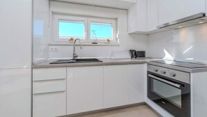 A modern kitchen with white cabinets, a double sink, a microwave, and a built-in oven. - Nova Excellence apartment (Novalja)