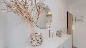 A white reception desk with a mirror, a vase with branches, and a small sculpture. - Nova Excellence apartment (Novalja)