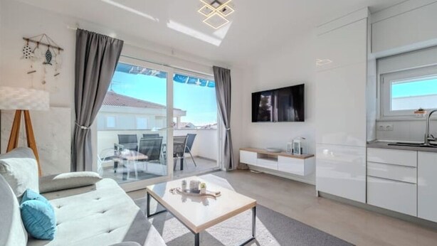 A modern living room with a sofa, coffee table, and a view of the outdoors through large windows. - Nova Excellence apartment (Novalja)