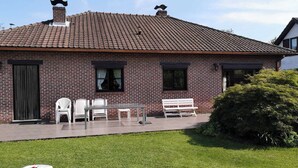 A brick house with a tiled roof, a front porch with a bench and chairs, and a small lawn area. - Vacation home Bornem, quiet location. Close to Ghent, Antwerp, Mechelen, Puurs (Bornem)