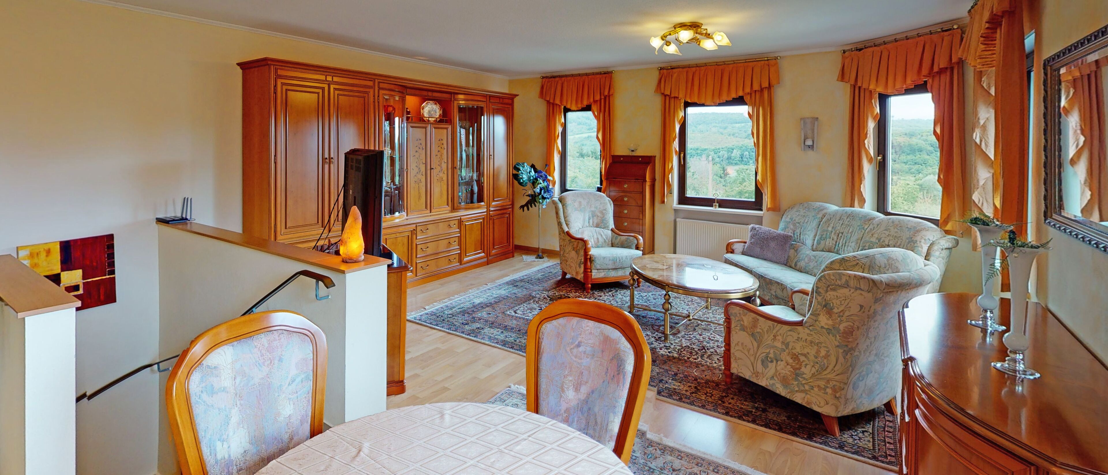 Ein geräumiges Wohnzimmer mit Sofa, Sesseln, einem Esstisch und einer Küchenzeile mit Holdekor.