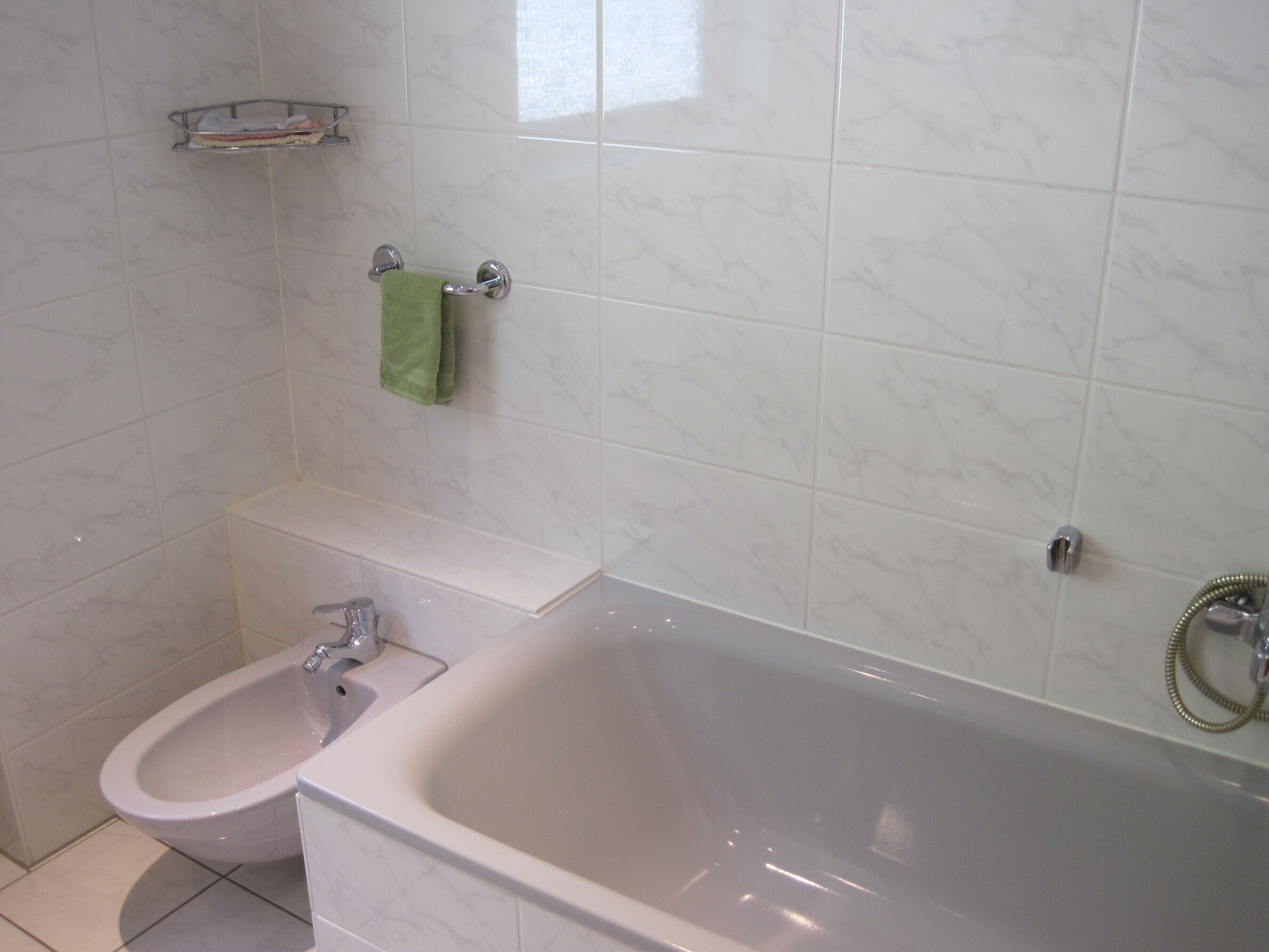 A bathroom with a bidet, a bathtub, and a towel rack with a green towel.