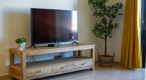 A flat-screen TV on a wooden TV stand with drawers, a small potted plant, and a tall indoor tree. - Apartment Ouravale - By D´alma (Albufeira)