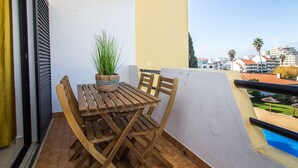 En balkon med et træbord og stole, en potteplante og udsigt til bygninger og palmer.