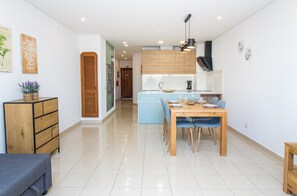A modern kitchen with wooden cabinets, a dining table with chairs, and a small side table. - Apartment Ouravale - By D´alma (Albufeira)