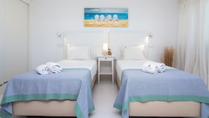 Une chambre d’hôtel avec deux lits, un tableau représentant des chaises de plage, une table de chevet avec une lampe et des serviettes sur les lits.