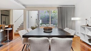 A modern dining area with a large table, six chairs, a kitchen area with a refrigerator, and a staircase leading to an outdoor patio. - Walk to Beach Coastal Home in Coogee (Perth)