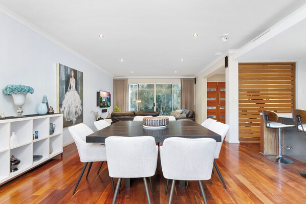 Uma sala de jantar moderna com uma mesa grande, cadeiras brancas e piso de madeira.