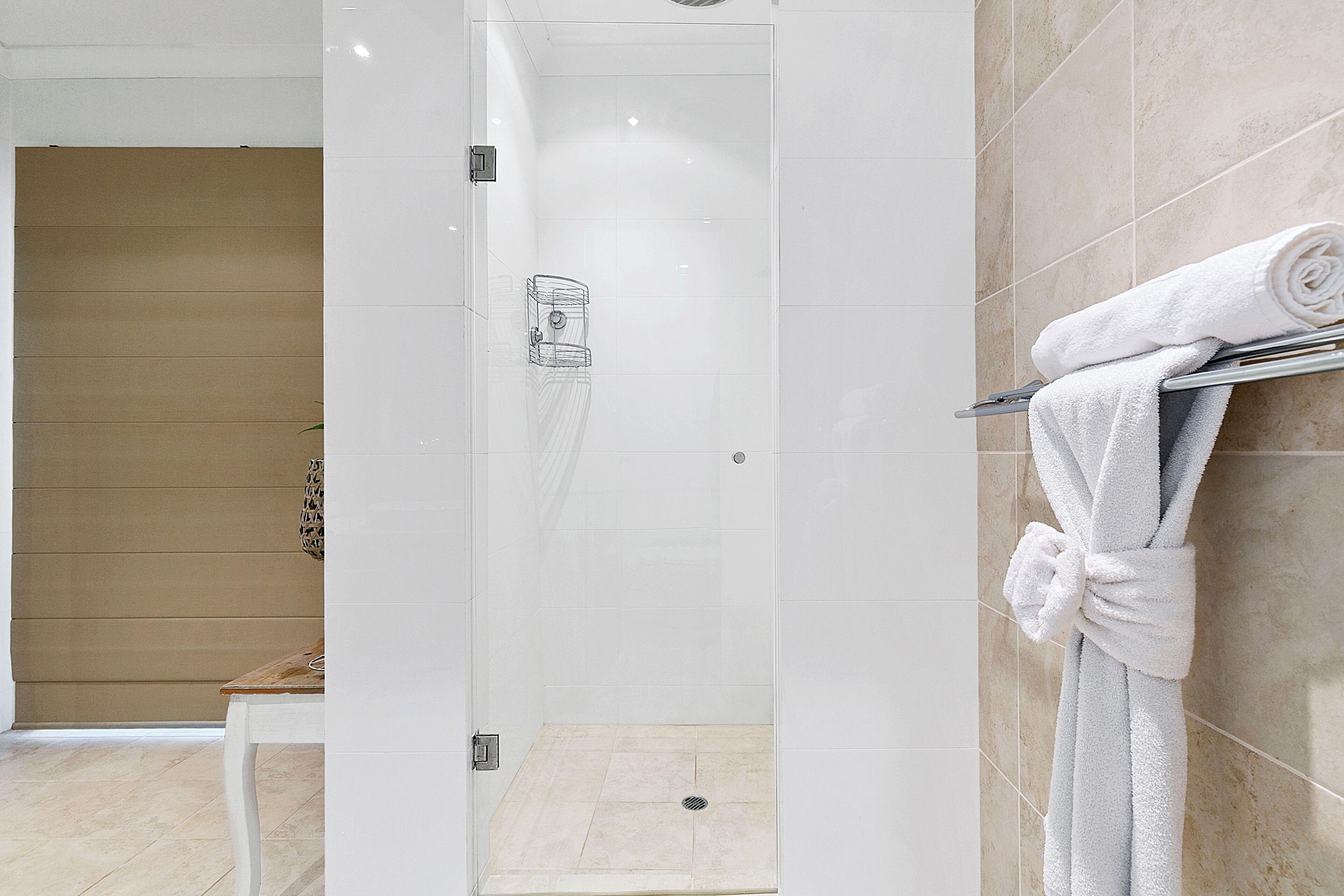 A modern bathroom with a glass-enclosed shower, a wooden bench, and a towel rack with a rolled towel.