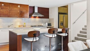 A modern kitchen with wooden cabinets, a stainless steel range hood, and a central island with bar stools. - Walk to Beach Coastal Home in Coogee (Perth)