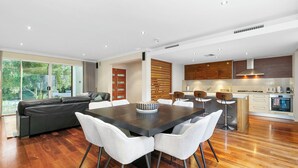 A modern kitchen with wooden cabinets, a central island, and a dining area with a dark table and white chairs. - Walk to Beach Coastal Home in Coogee (Perth)