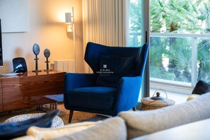 Ein modernes Wohnzimmer mit blauem Sessel, einer Holzkommode und Blick ins Grüne.