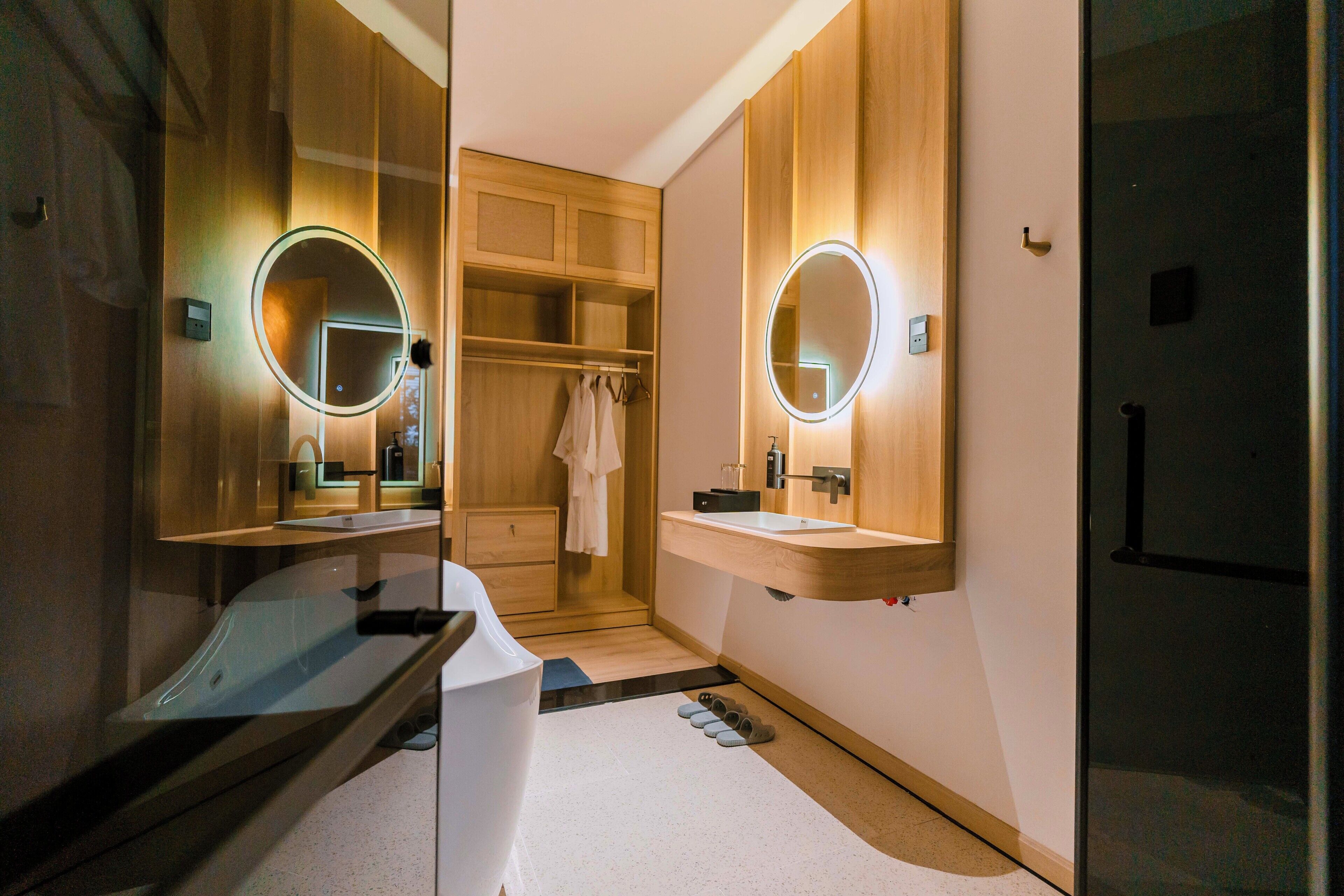 Un baño moderno con dos lavabos, armarios de madera e iluminación integrada en el espejo.