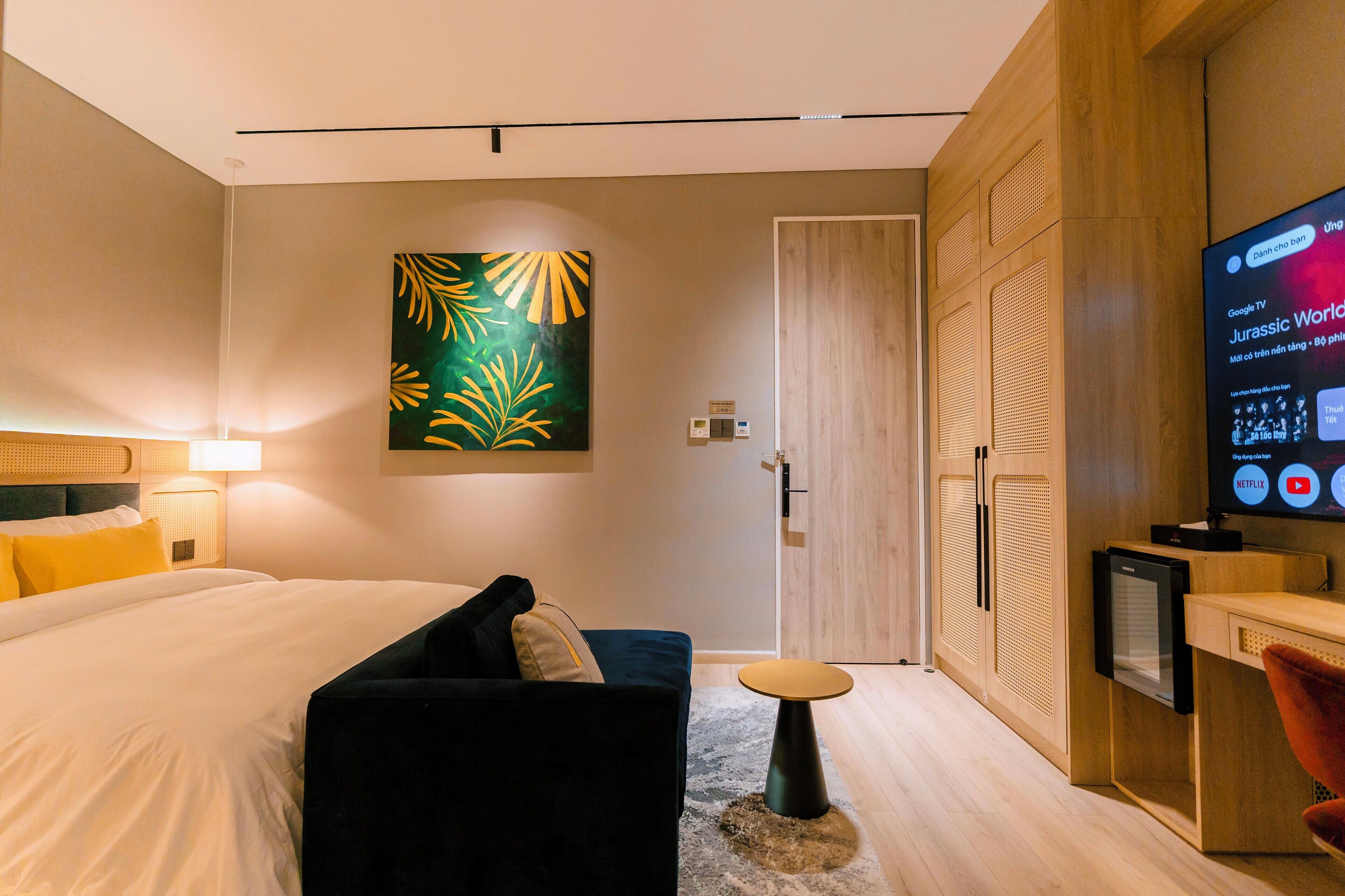 A modern hotel room with a bed, a sofa, a TV, and a wardrobe.