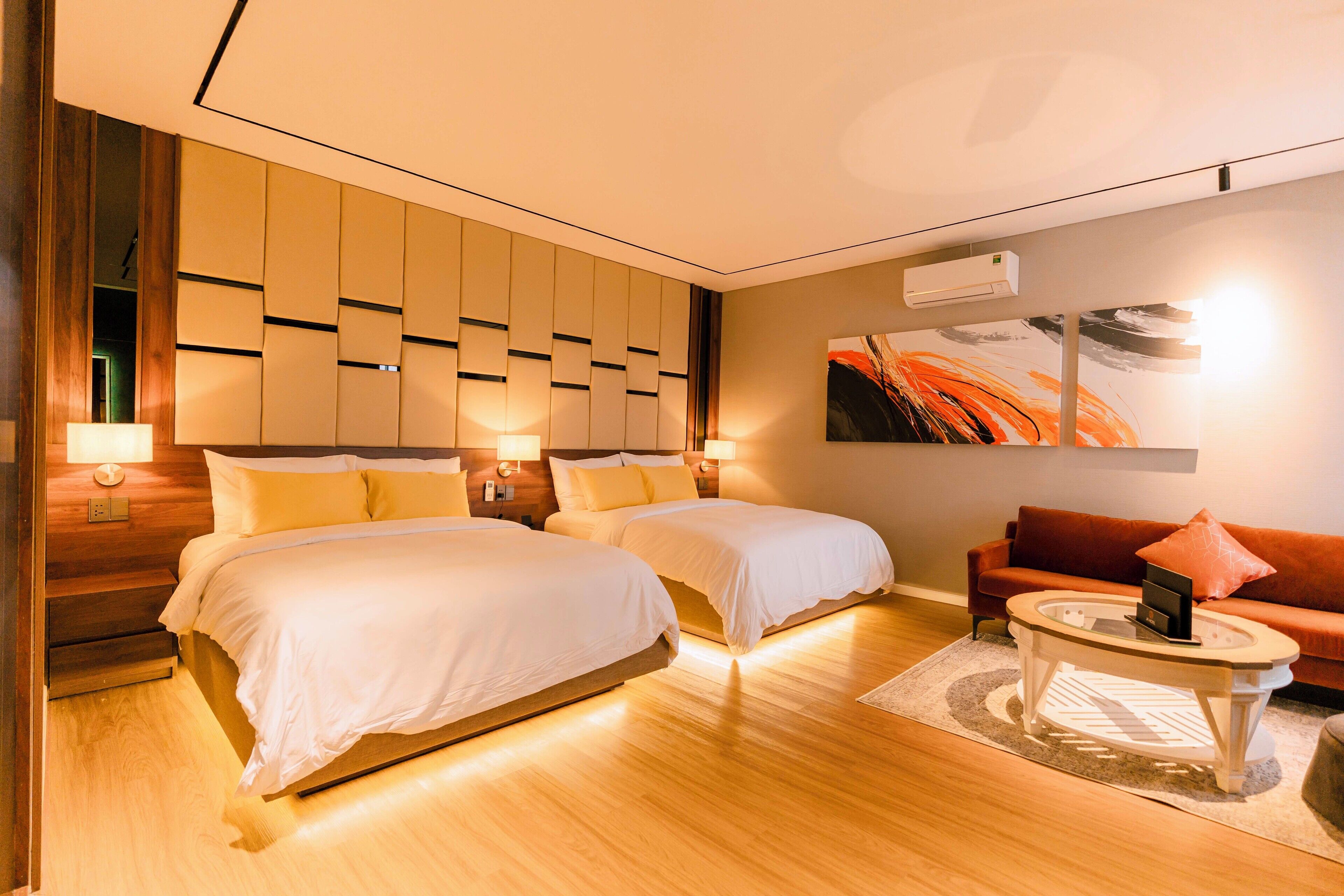 A hotel room with two beds, a sofa, a coffee table, and a painting on the wall.