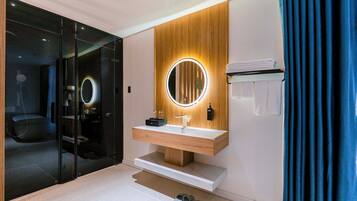 A modern bathroom with a wooden vanity, a round mirror with a light, and a glass shower enclosure.