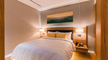 A modern hotel room with a large bed, wooden headboard, bedside lamps, and a painting on the wall.