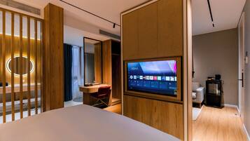 Ein modernes Hotelzimmer mit einem großen Bett, einem an einer Holzvertäfelung befestigten Fernseher, einem Schreibtisch mit Stuhl und einer kleinen Küchenzeile.