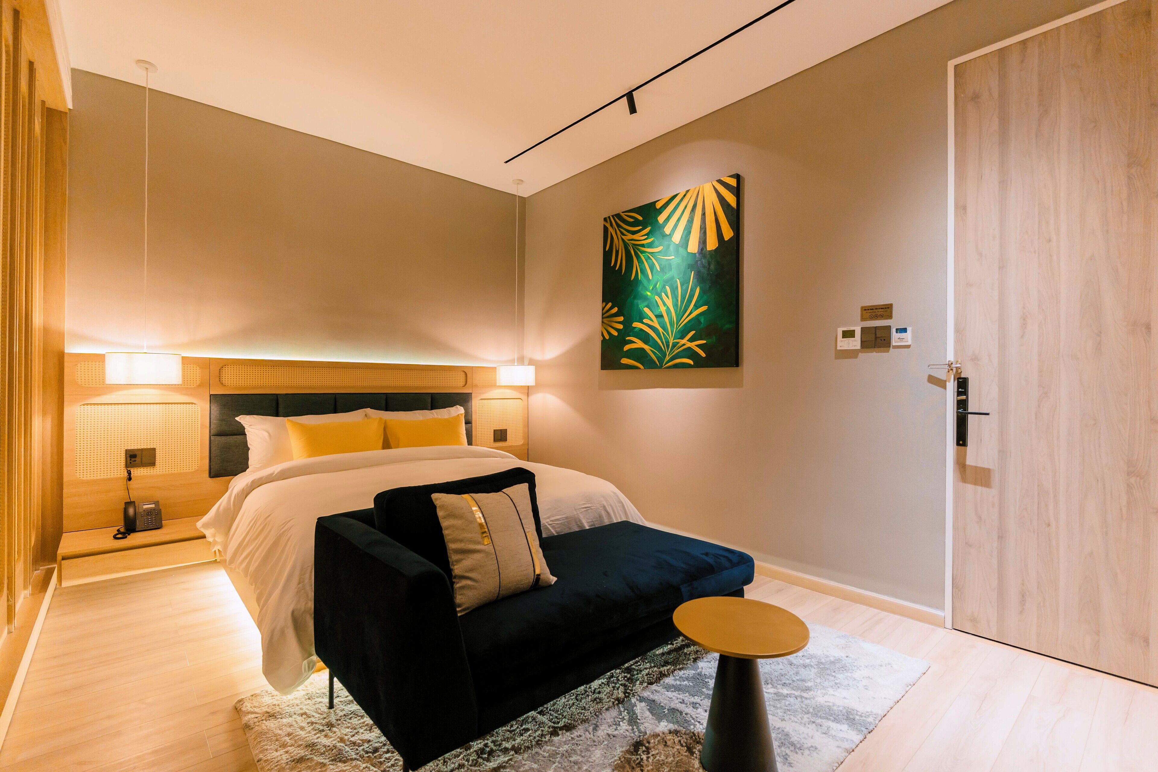 A modern bedroom with a bed, bedside lamps, a sofa, a round table, and a painting on the wall.