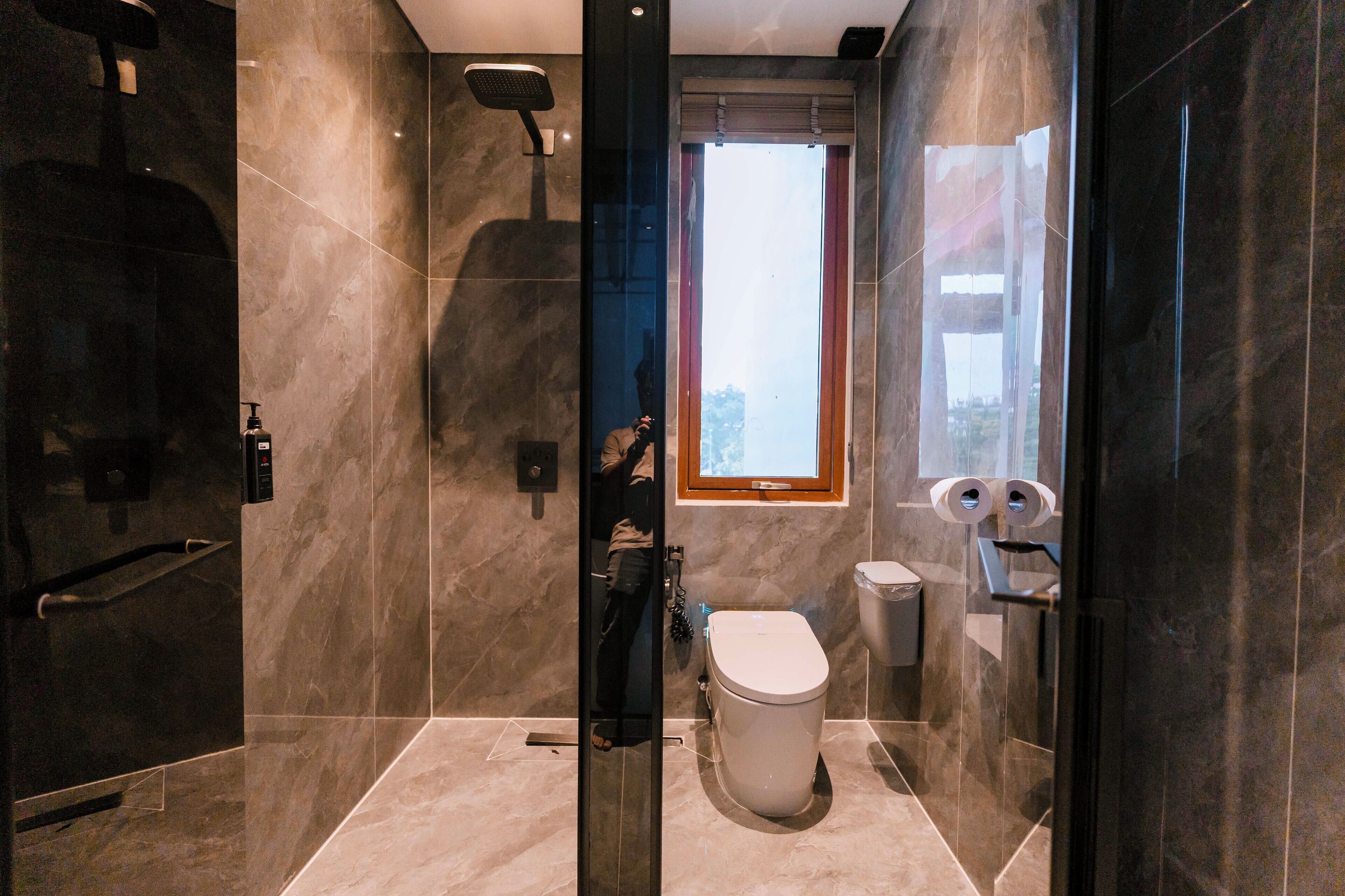 A modern bathroom with a glass-enclosed shower, a toilet, and a window providing natural light.