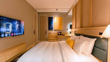 A hotel room with a large bed, a TV mounted on the wall, a wooden headboard, and a bedside table.