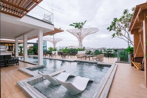 A rooftop pool area with modern seating, a bar, and a view of the cityscape. - JA Hotel (Rach Gia)