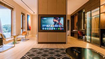 A modern living room with a large flat-screen TV mounted on a wooden panel, a black and white patterned rug, and contemporary furniture including a sofa and chairs.