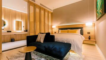 A modern hotel room with a bed, bedside table, and a seating area with a sofa.