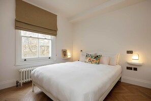 Une chambre avec un grand lit, une fenêtre donnant sur un beau paysage, un radiateur et des lampes fixées au mur.