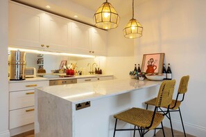 A modern kitchen with white cabinets, a marble island, and two hanging pendant lights. - A Joyful Abode, by Veeve (London)