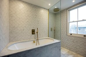 Une salle de bain moderne avec une baignoire sur pieds, un grand miroir et une fenêtre donnant sur l’extérieur.
