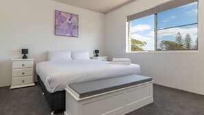 Un dormitorio con cama, mesitas de noche, un banco, una ventana con vistas y una obra de arte en la pared.