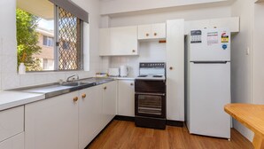 Una cocina compacta con gabinetes blancos, horno empotrado, refrigerador y ventana con mosquitero.