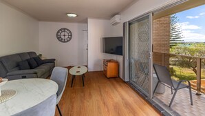 Un balcón con televisor, sofá, una mesita y una silla.