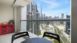 A balcony with a table and chairs, a red cabinet, and a view of a cityscape with tall buildings. - 2304 (Dubai)
