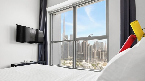 A hotel room with a large window, a flat-screen TV, a bed, and a bedside table. - 2304 (Dubai)