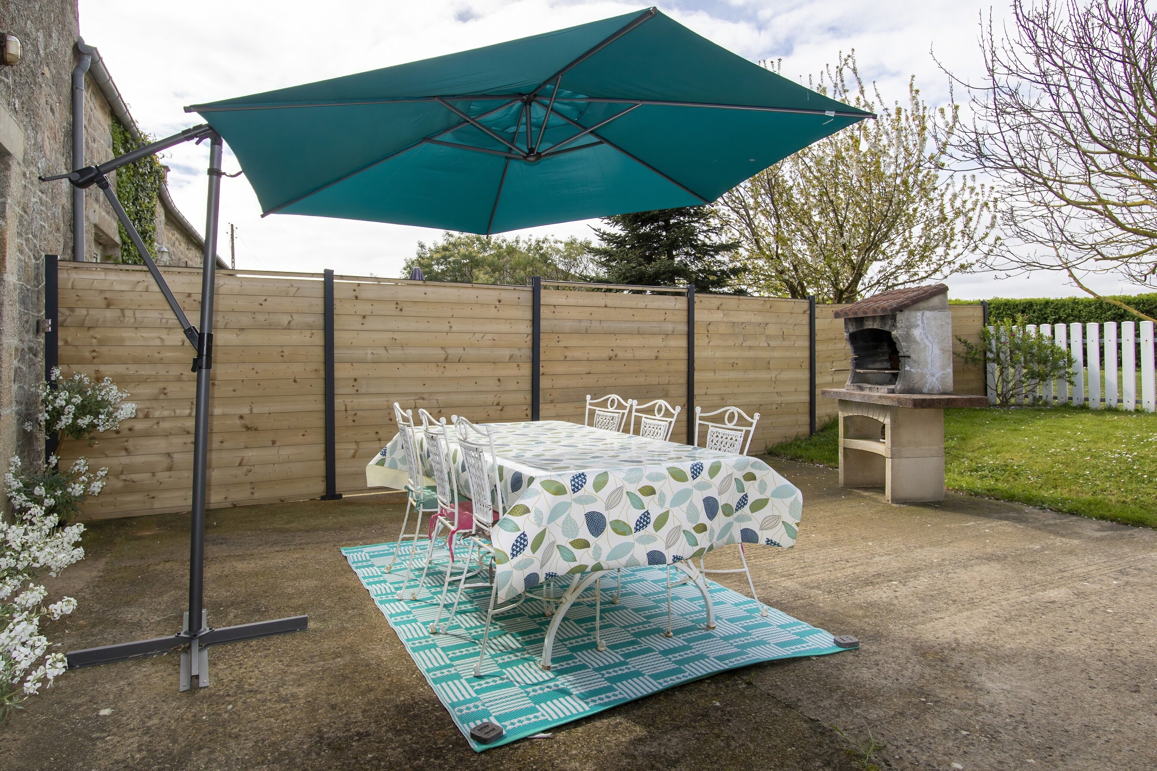 Eine Terrasse mit Tisch und Stühlen, einem grünen Sonnenschirm und einem Grill.