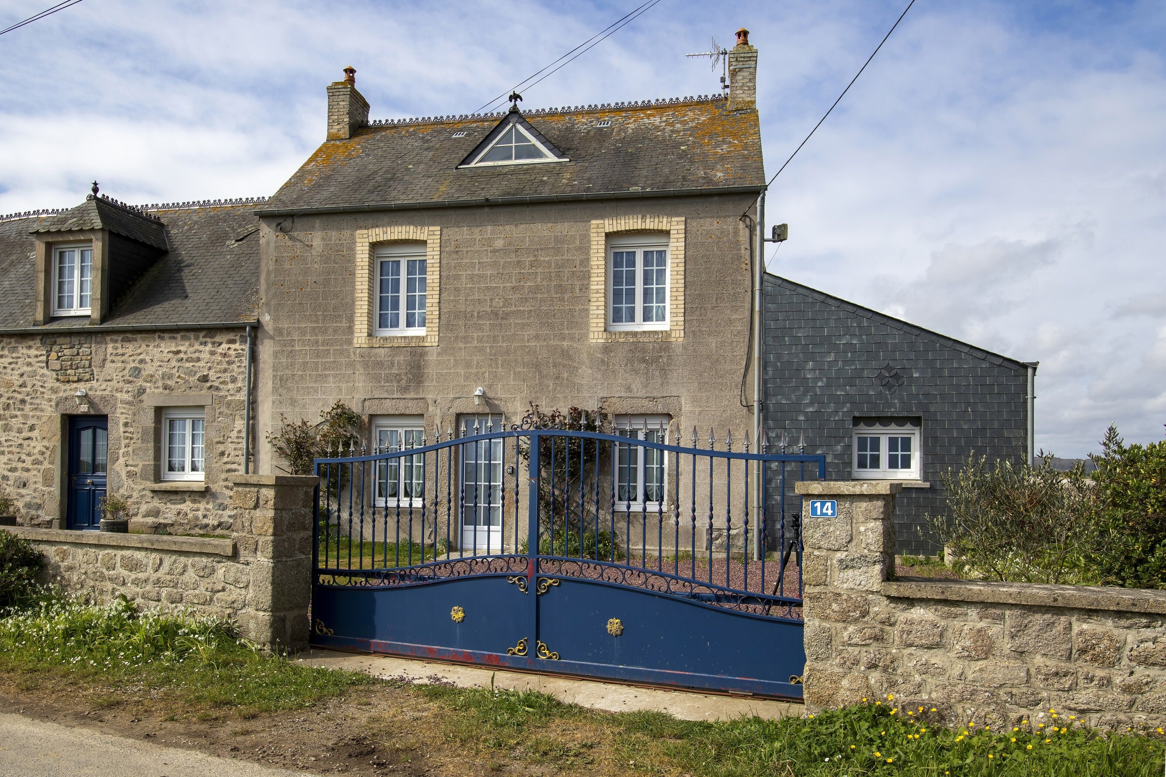 A stone house with a blue gate, numbered 14, and a small garden.