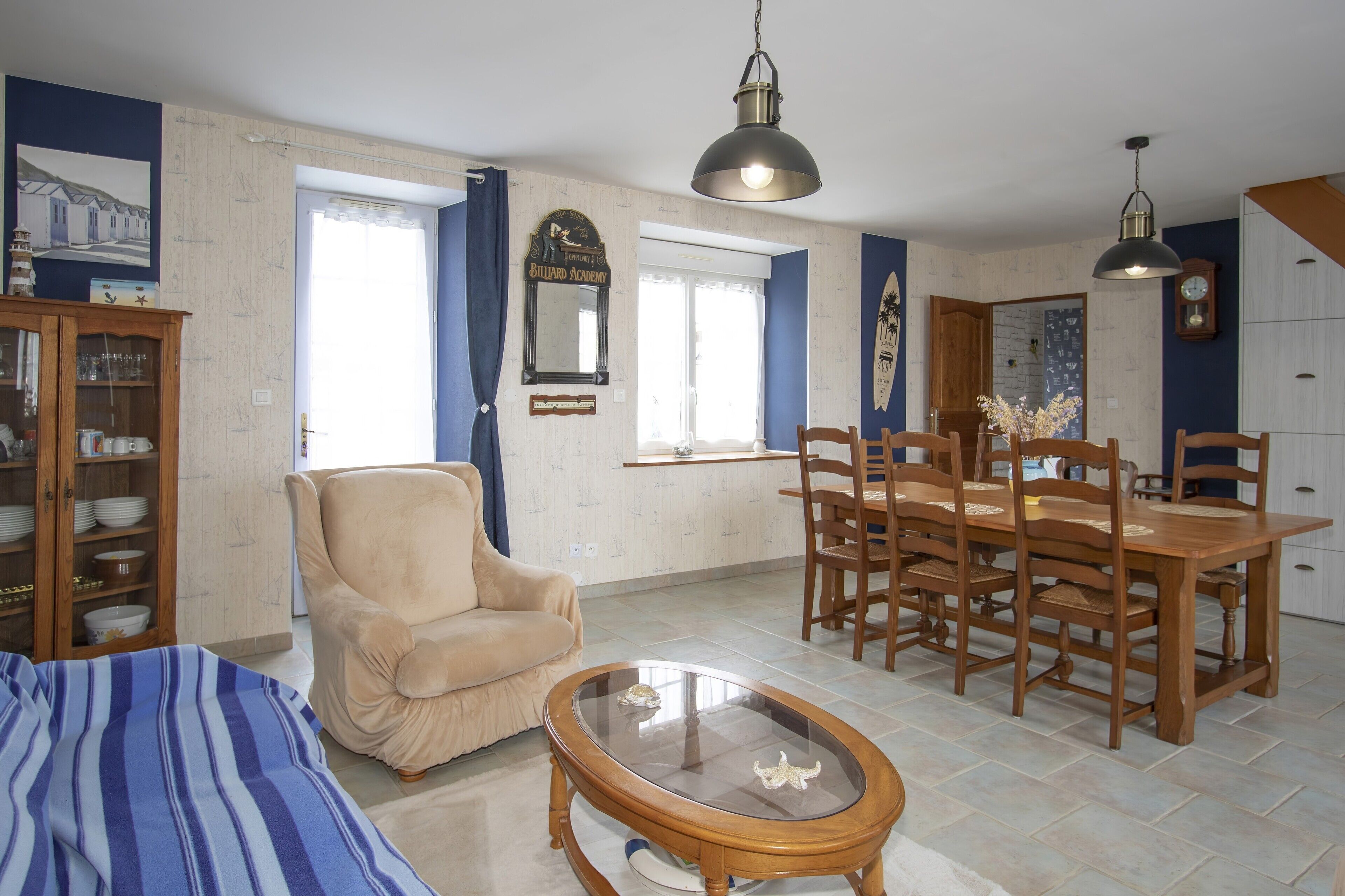 Una sala de estar con sofá, mesa de centro, mesa de comedor con sillas, candelabro y un reloj en la pared.