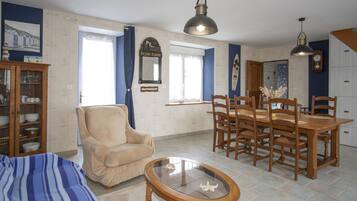 Una sala de estar con sofá, mesa de centro, mesa de comedor con sillas, candelabro y un reloj en la pared.