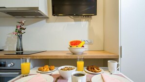 Et morgenmåltidsbord med tallerkener, skåle og glas, et ur og et fjernsyn hængende over.