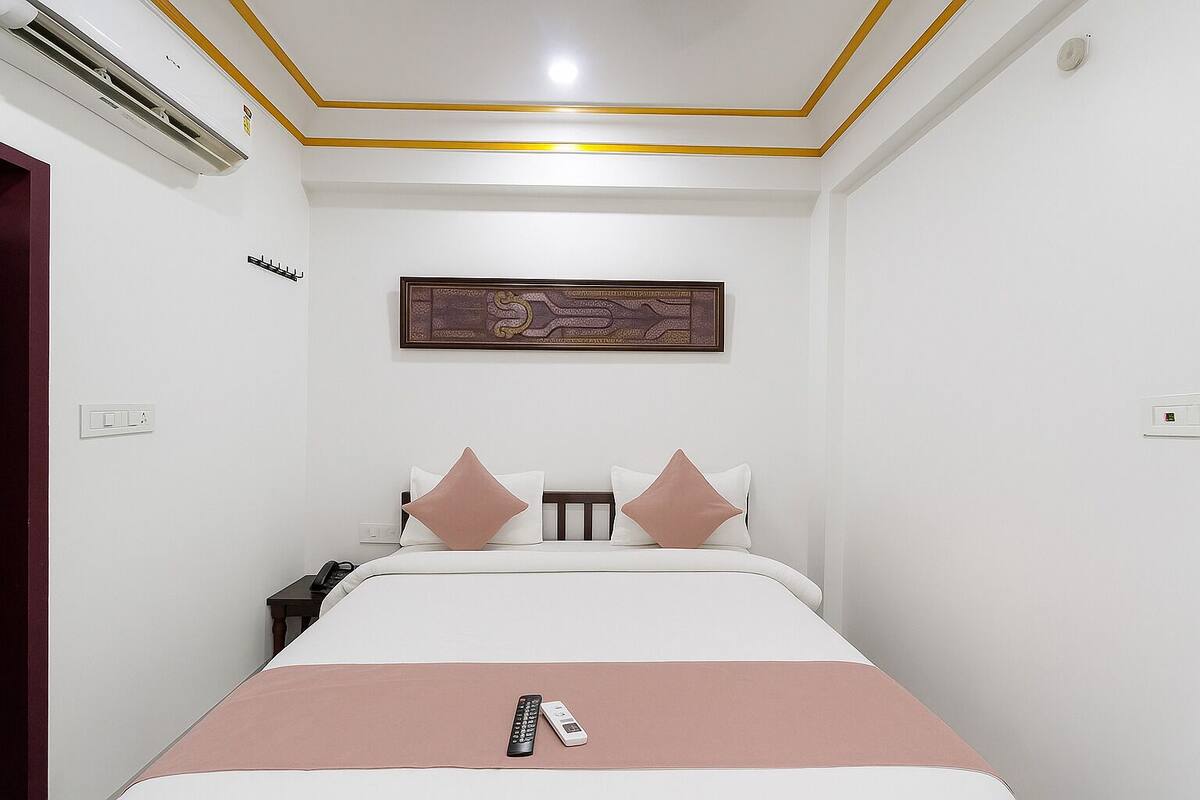A hotel room with a bed, a nightstand, a phone, and a remote control on the bed.
